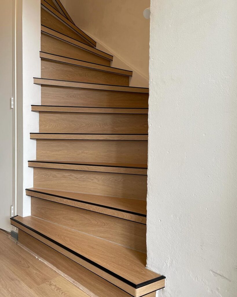 Traprenovatie Deurne: Een trap met houtlook PVC bekleding die een moderne, stijlvolle en warme ambiance creëert na de renovatie.